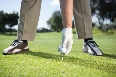 Golfer placing golf ball on tee on a sunny day at the golf courseの写真素材