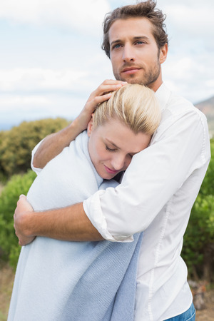 Protective man hugging his girlfriend in blue blanket outside on a chilly dayの写真素材