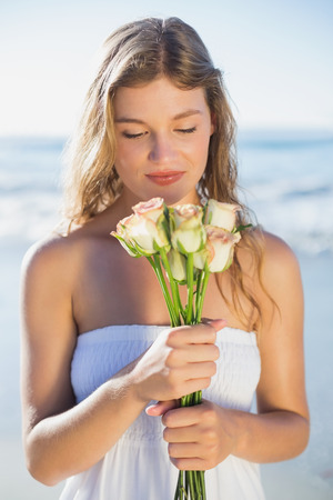 Beautiful blonde in sundress smelling roses on the beach on a sunny dayの写真素材