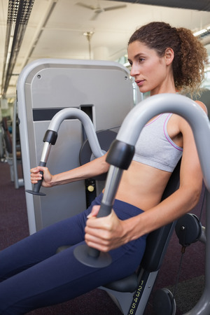 Fit woman using the weights machine for her arms at the gym