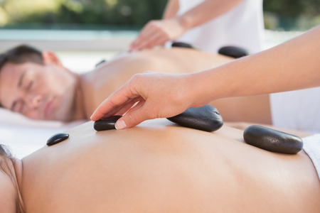 Attractive couple enjoying hot stone massage poolside outside at the spaの写真素材