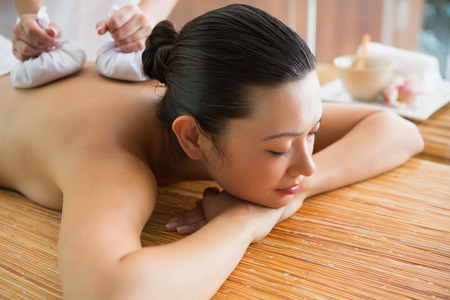 Smiling brunette getting a herbal compress massage at the health spaの写真素材
