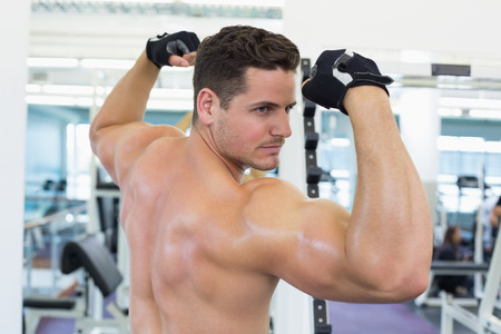 Shirtless bodybuilder flexing his biceps at the gym