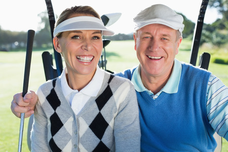 Happy golfing couple sitting in golf buggy smiling at camera on a sunny day at the golf courseの写真素材
