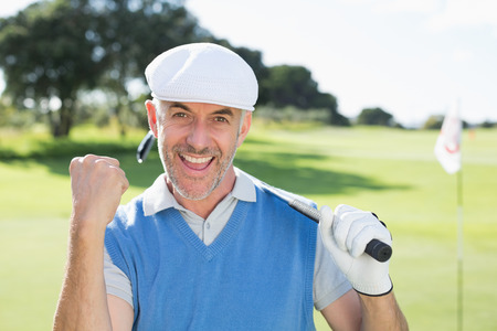 Happy golfer cheering at camera on putting green on a sunny day at the golf courseの写真素材