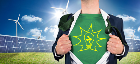 Businessman opening shirt in superhero style against large solar panel and three wind turbinesの写真素材