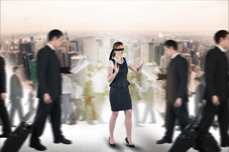 Composite image of redhead businesswoman in a blindfold walking through crowdの写真素材