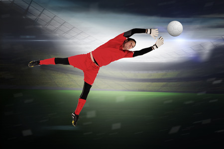 Fit goal keeper jumping up in a large football stadium with lightsの写真素材