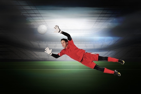 Fit goal keeper jumping up in a large football stadium with lightsの写真素材