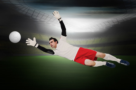 Goalkeeper in white making a save in a large football stadium with lightsの写真素材