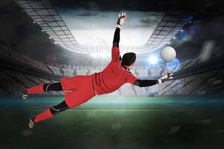 Fit goal keeper jumping up in a large football stadium with lightsの写真素材