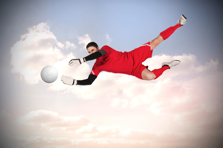 Fit goal keeper jumping up against beautiful blue cloudy skyの写真素材