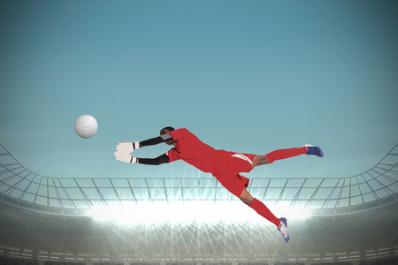 Goalkeeper in red making a save against large football stadium with spotlightsの写真素材