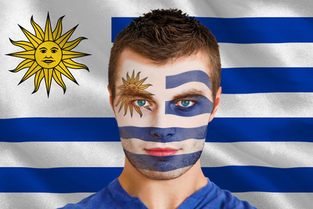 Composite image of serious young uruguay fan with facepaint against digitally generated uruguay national flagの写真素材