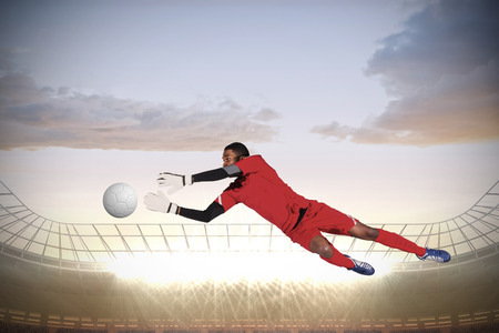 Goalkeeper in red making a save against large football stadium with spotlightsの写真素材