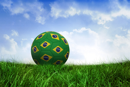 Football in brazilian colours on field of grass under blue skyの写真素材