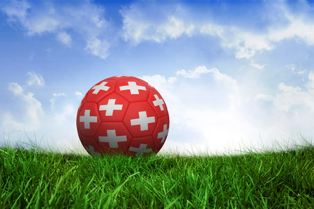 Football in switzerland colours on field of grass under blue skyの写真素材