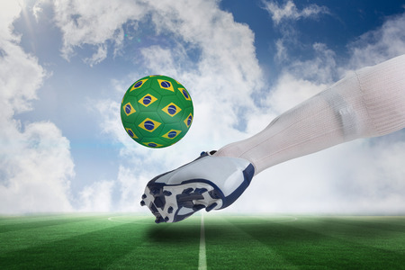 Composite image of close up of football player kicking brasil ball against football pitch under blue skyの写真素材