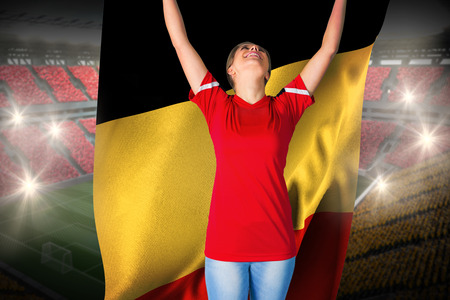Cheering football fan in red holding belgium flag against vast football stadium with fans in yellow and redの写真素材