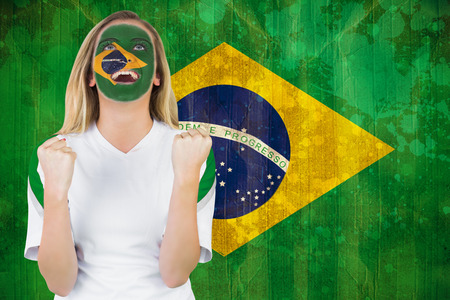 Excited brasil fan in face paint cheering against brazil flag in grunge effectの写真素材