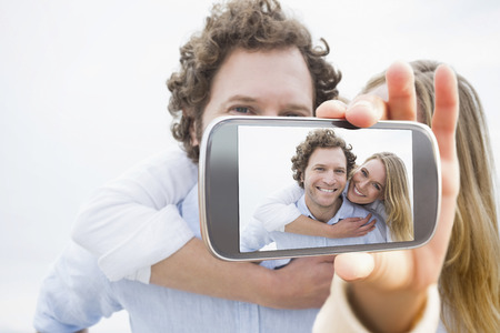 Hand holding smartphone showing man piggybacking woman at beach