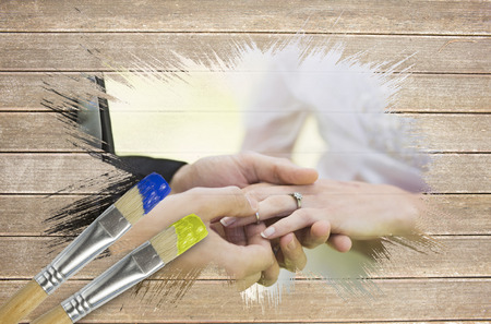 Composite image of groom placing ring on brides finger with paintbrush dipped in yellow against wooden surface with planksの写真素材