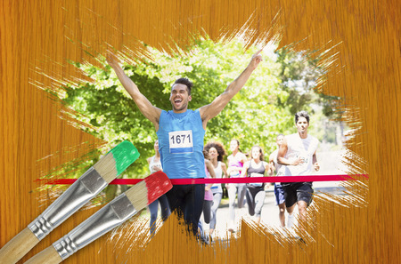 Composite image of racer crossing finishing line with paintbrush dipped in red against wooden pine tableの写真素材