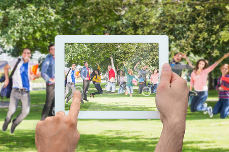 Hand holding tablet pc showing college students jumping in the parkの写真素材