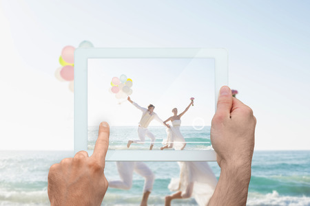 Hand holding tablet pc showing newlyweds having fun holding balloonsの写真素材