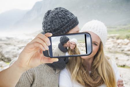 Hand holding smartphone showing man kissing a woman on rocky landscapeの写真素材