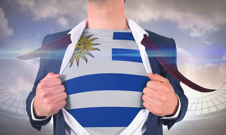 Businessman opening shirt to reveal uruguay flag against large football stadium under cloudy blue skyの写真素材