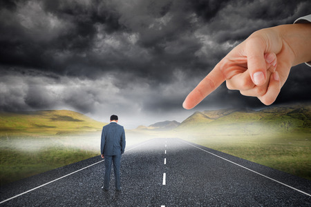 Giant hand pointing at businessman standing against stormy landscape background with streetの写真素材
