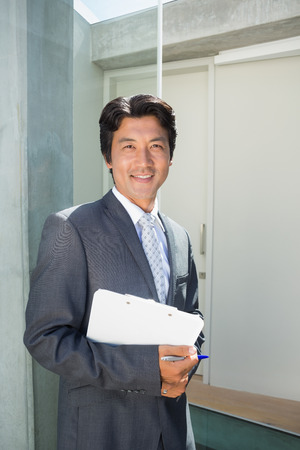 Confident estate agent standing at front door with clipboard outside a houseの写真素材