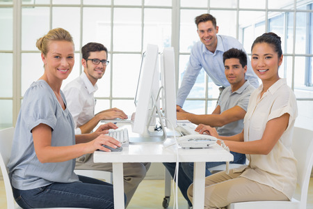 Casual business team smiling at camera at desk in the office