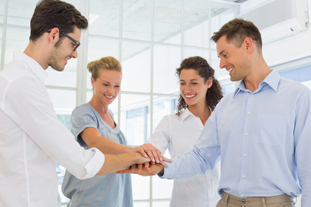 Casual business team putting their hands together in the office