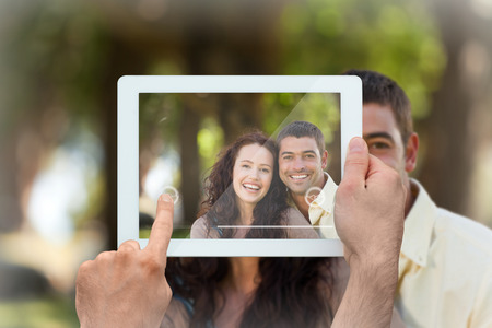 Hand holding tablet pc showing couple sitting in the gardenの写真素材