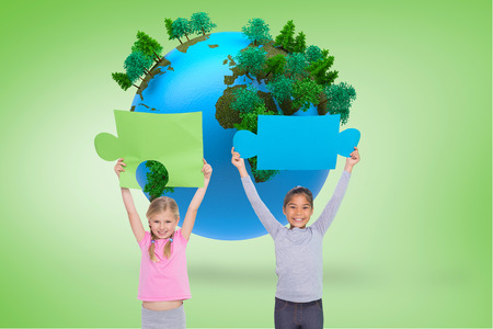Elementary pupils holding jigsaw pieces against green vignette with globeの写真素材