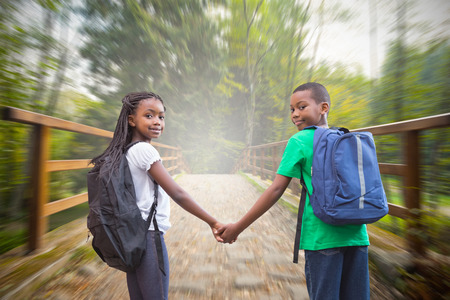 Cute pupils holding hands against bridge with railings leading towards forestの写真素材