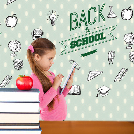 Cute girl using tablet against red apple on pile of booksの写真素材