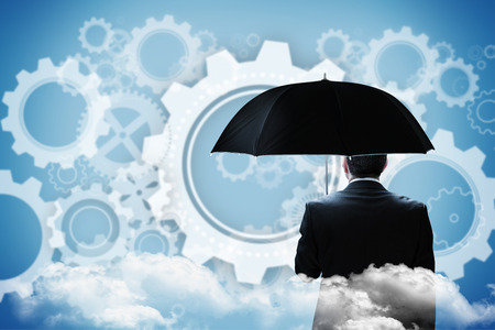 Mature businessman holding an umbrella against white wheels and cogs on blueの写真素材