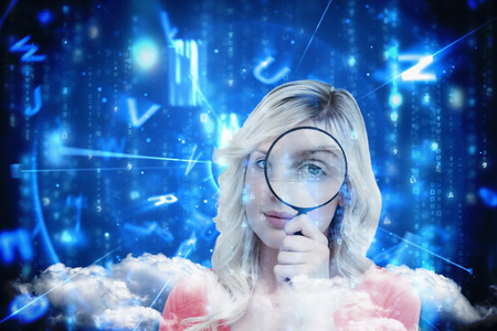 Fair-haired woman looking through a magnifying glass against lines of blue blurred letters fallingの写真素材
