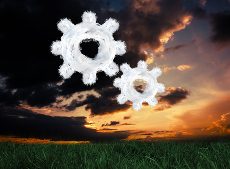 Cloud cog and wheel against green grass under dark blue and orange skyの写真素材