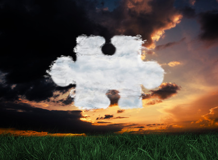 Cloud jigsaw piece against green grass under dark blue and orange skyの写真素材