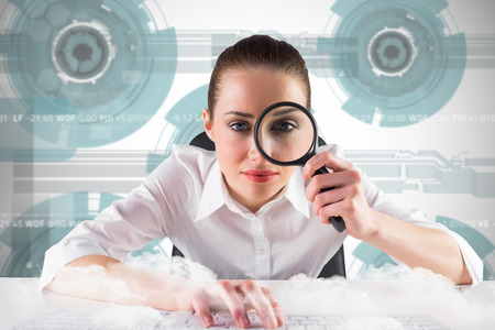 Businesswoman typing and looking through magnifying glass against technology wheel backgroundの写真素材
