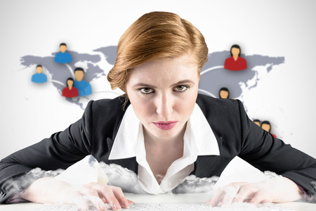 Redhead businesswoman sitting at desk typing against view of communication networkの写真素材
