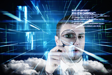 Businessman looking through magnifying glass against blue lines next to screens and textの写真素材
