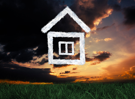 Cloud house against green grass under dark blue and orange skyの写真素材