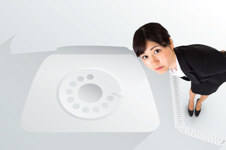 Serious businesswoman bending against retro telephone on greyの写真素材