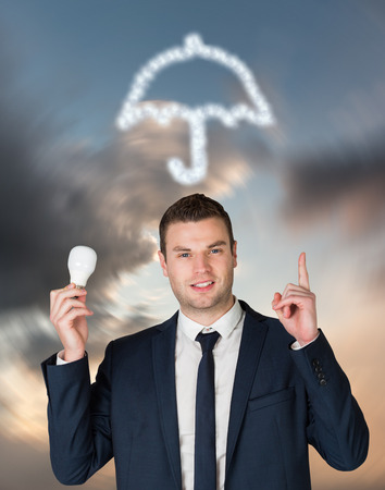 Businessman holding light bulb and pointing against blue and orange sky with cloudsの写真素材