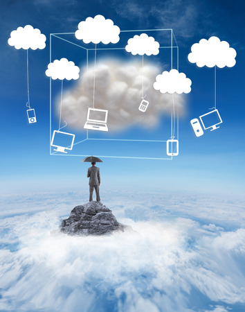 Businessman standing under umbrella against mountain peak through the cloudsの写真素材